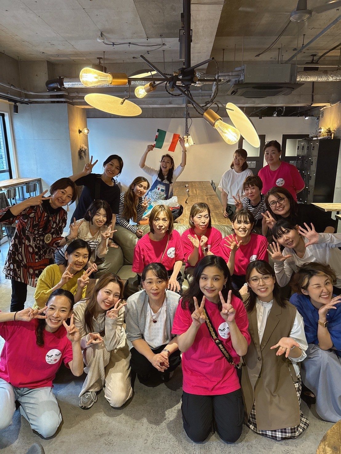 Group photo inside cafe filament: the organising team in matching pink T-shirts and the exhibitors, making peace signs